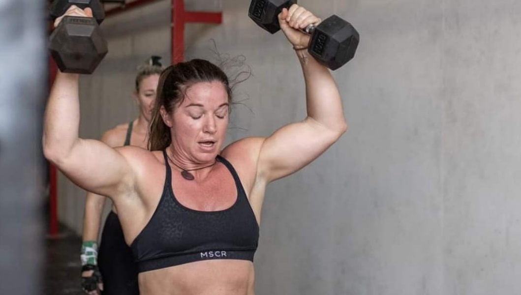 Naomi Lewin pressing dumbbells overhead in the gym